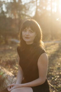 Picture of author Elisa Faison sitting on a fallen tree with the sun behind her.